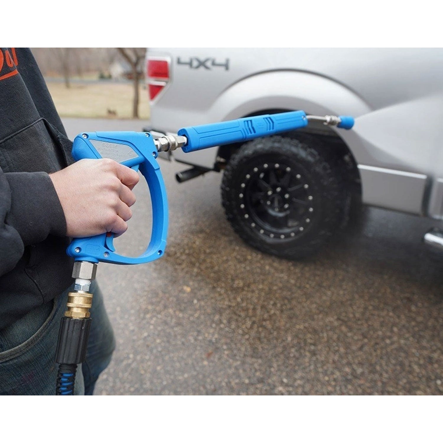 Person holding a blue pressure washer gun with a truck in the background