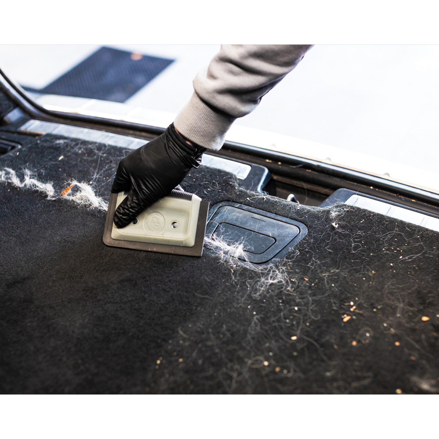 Person cleaning pet hair off of a car's black interior surface 