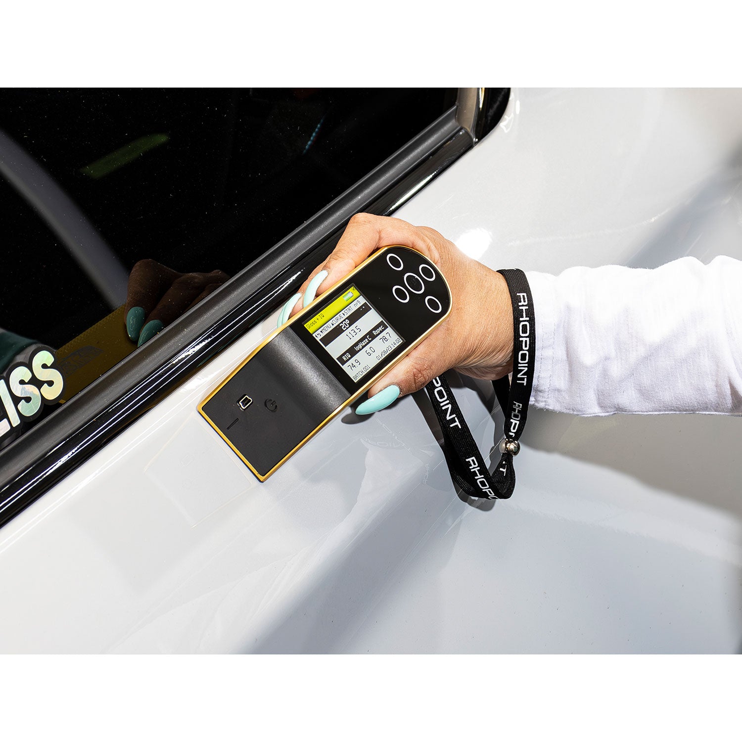 Hand holding a detailometer near a car window with a white background