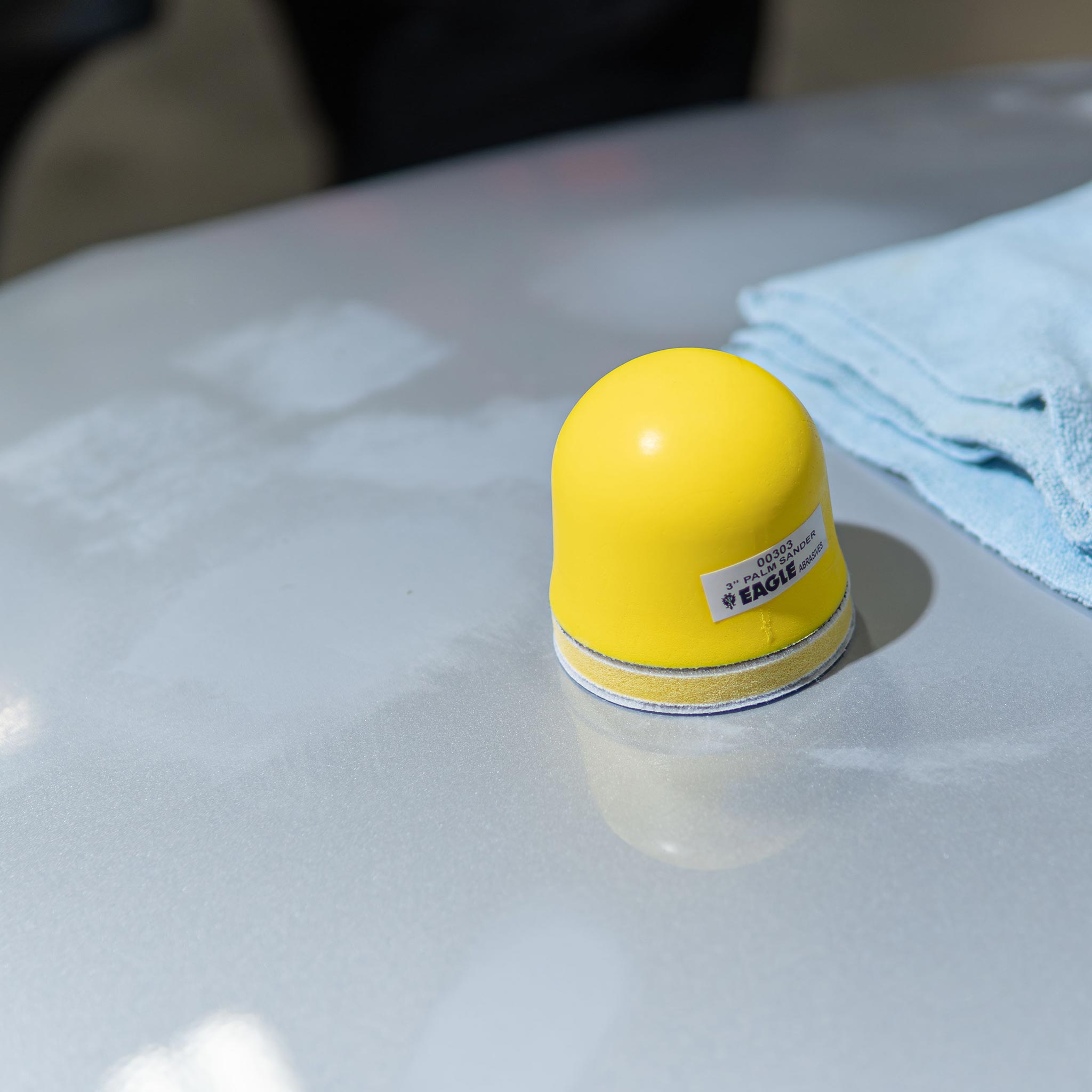Yellow palm anding tool on a silver car hood with a blue towel in the background