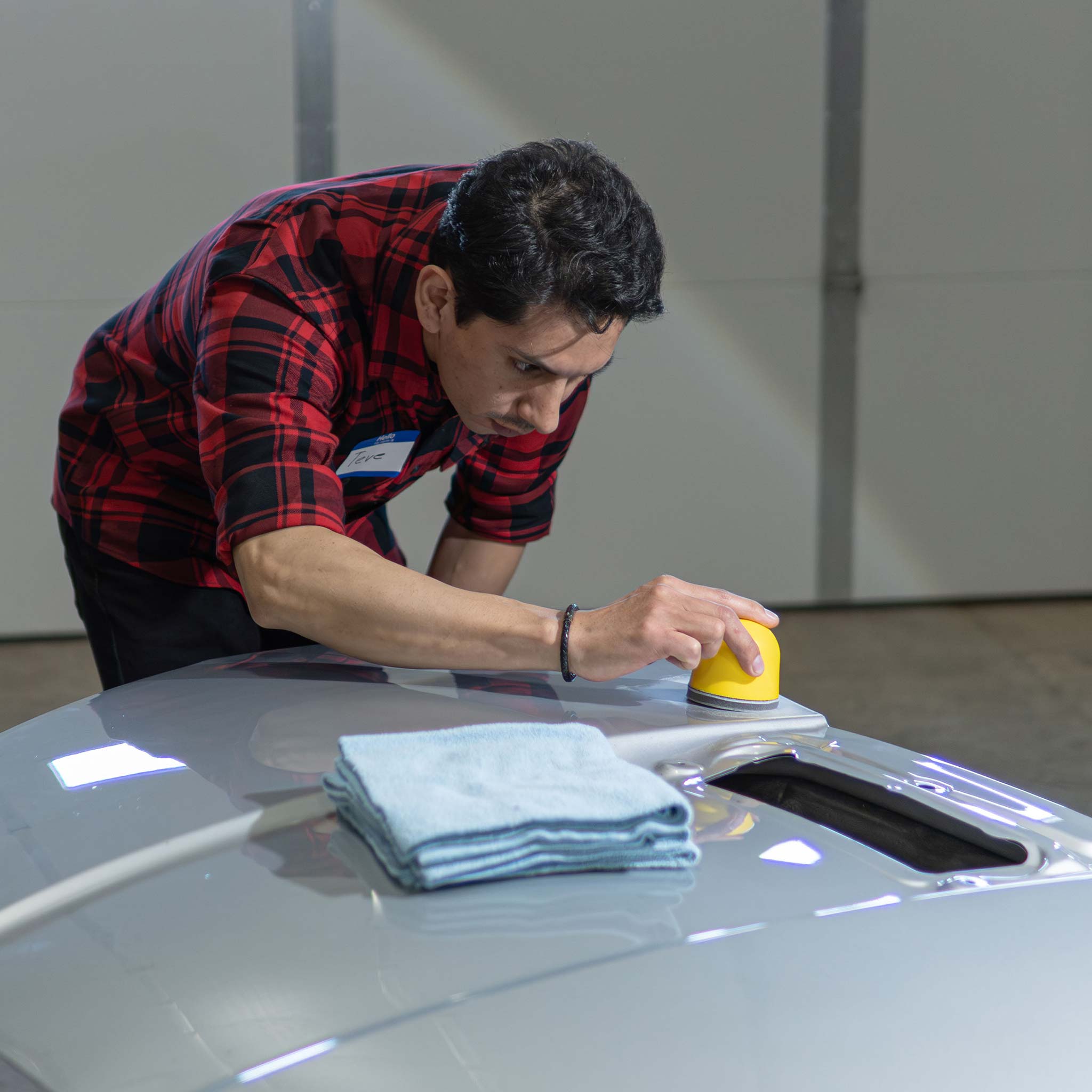 Person sanding a car hood with a yellow palm sander and blue towels