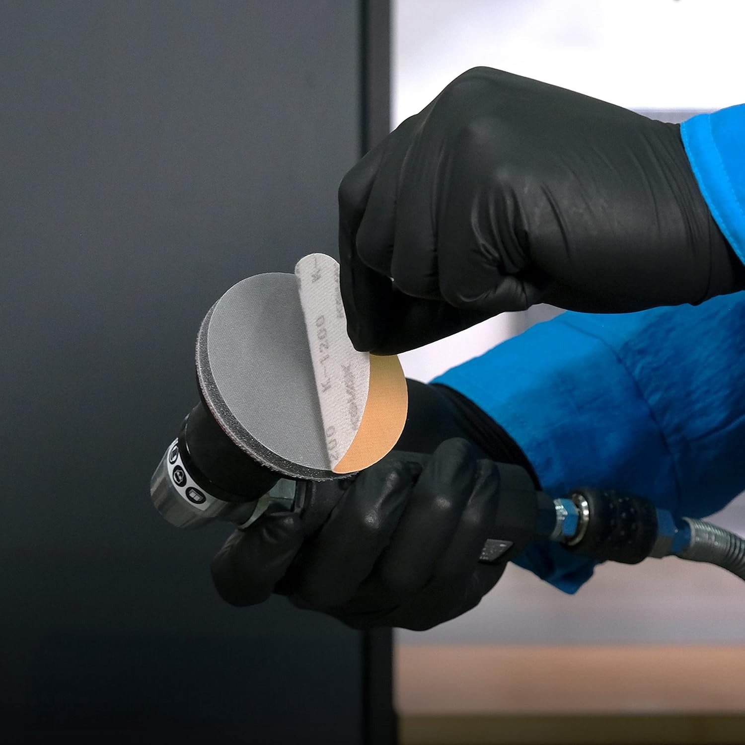 Person wearing black gloves holding a sanding tool against a dark surface