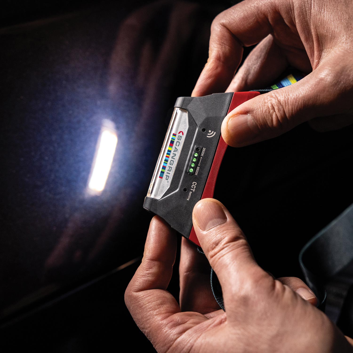 Person holding a Headlamp against a dark car paint background