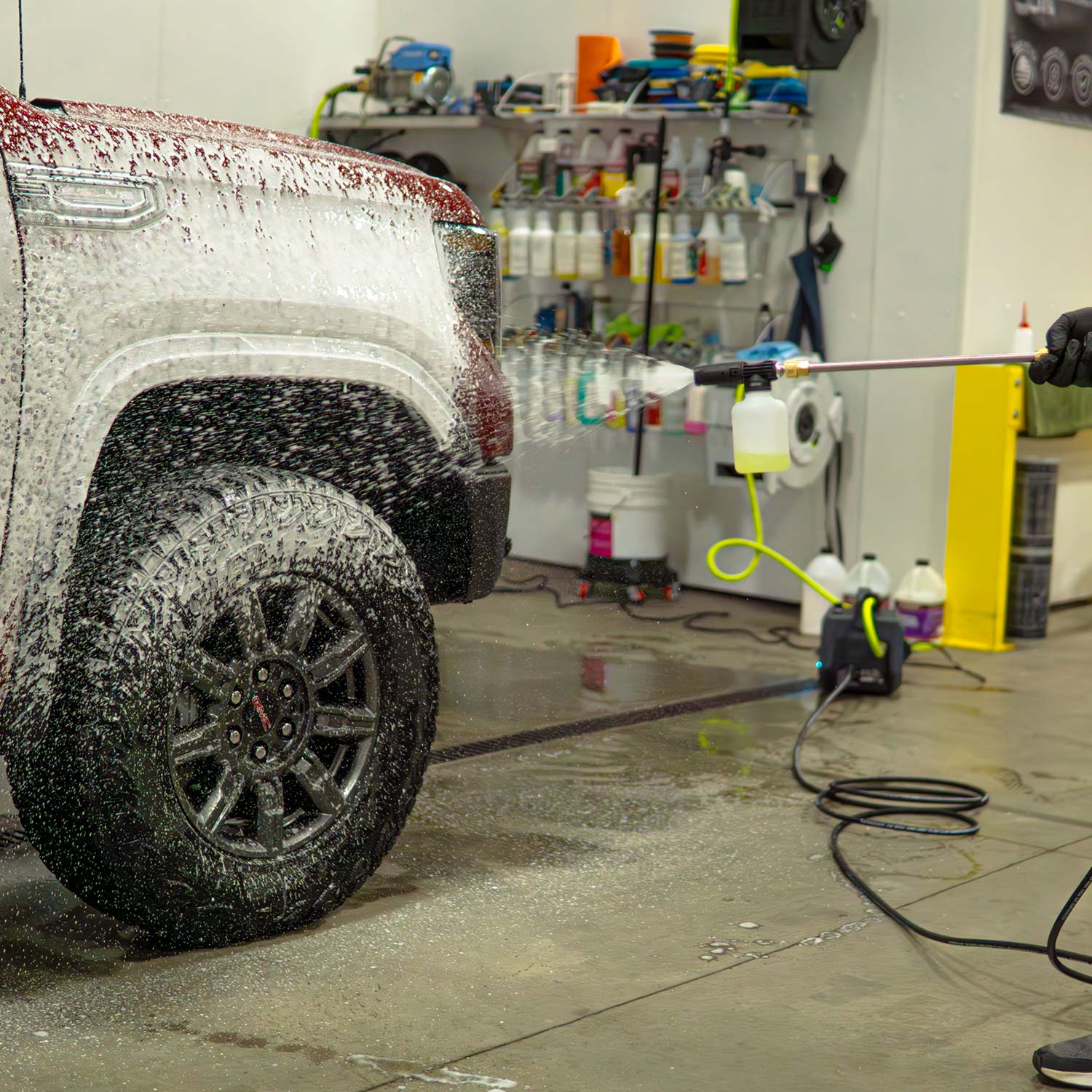 Car washing process with a vehicle covered in soap suds in a garage setting.