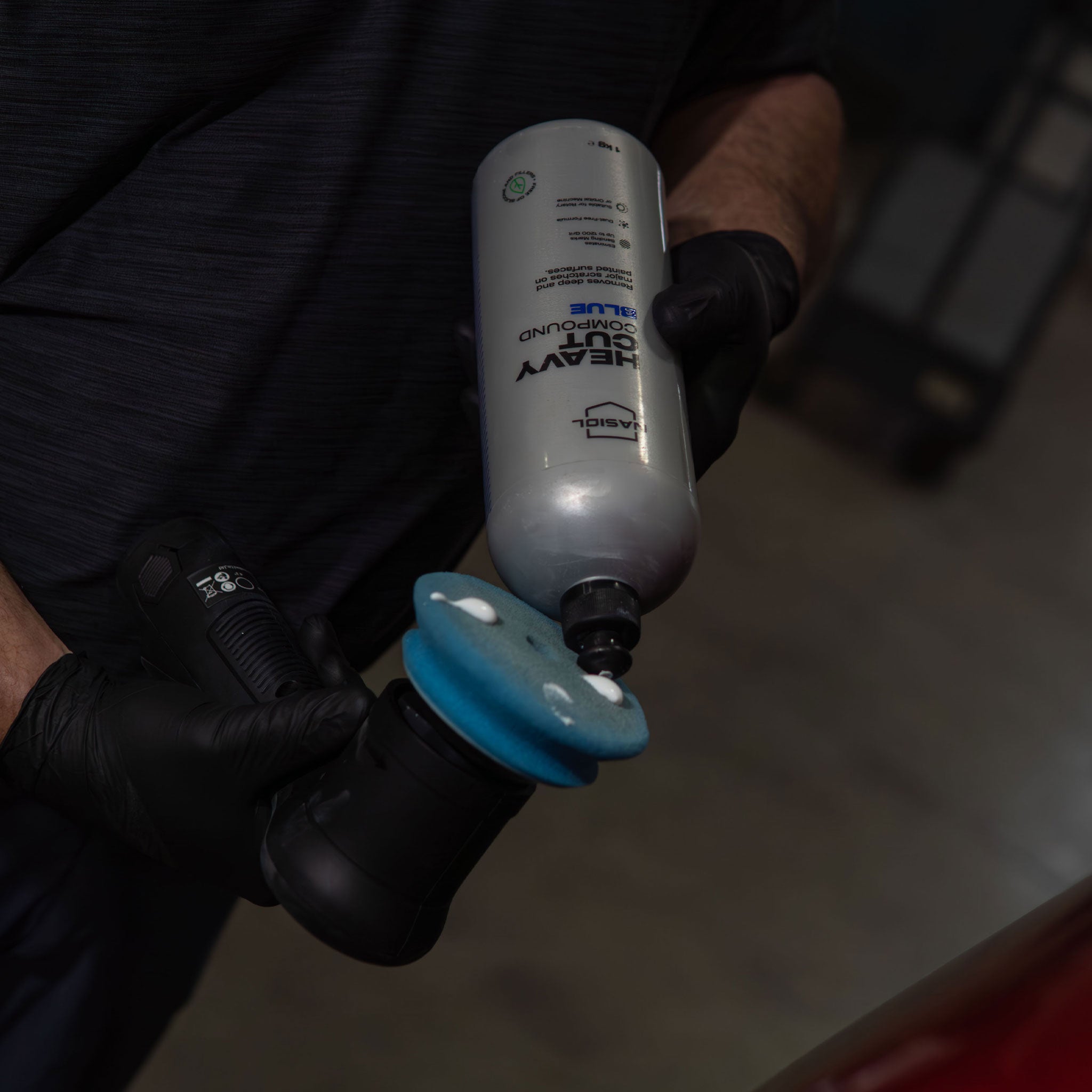 Person wearing black gloves holding a buffer with blue pad spreading heavy cut compound