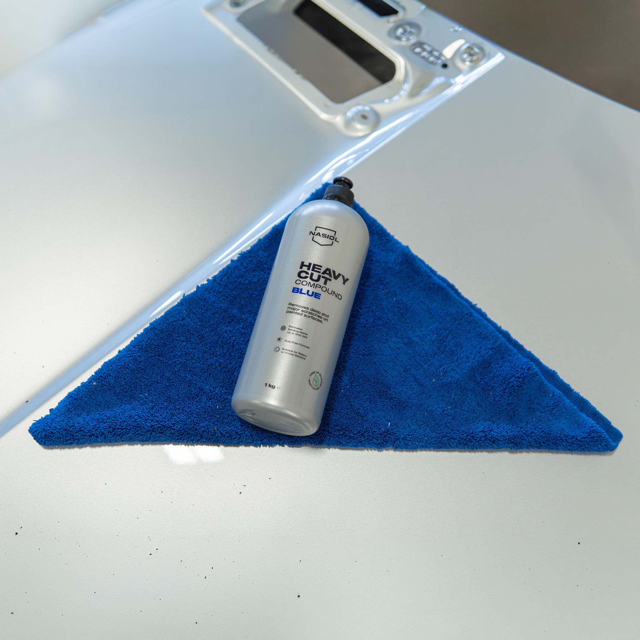 Bottle of car polish on a blue microfiber towel with a white car surface in the background