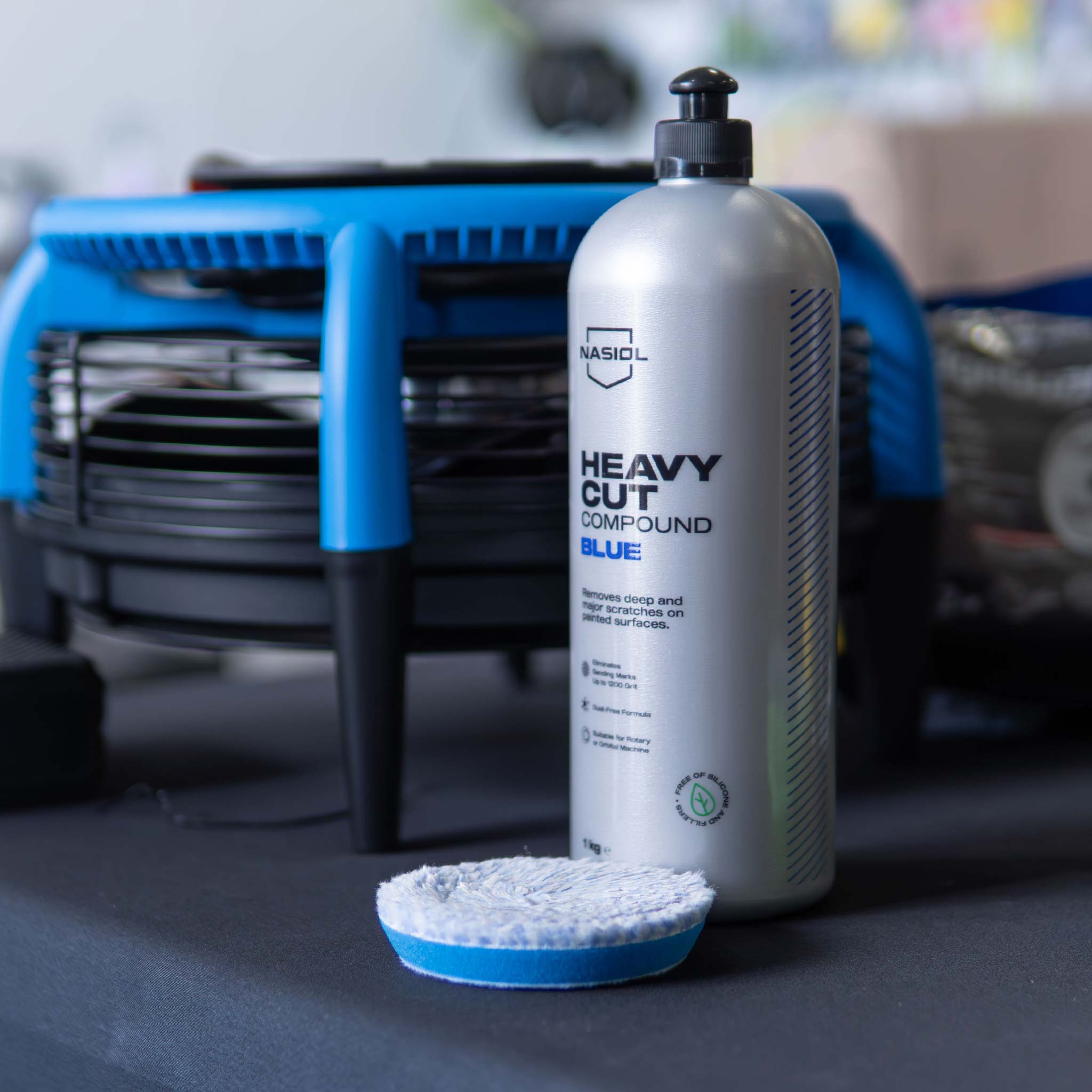 Car care product bottle labeled 'Heavy Cut Compound Blue' with a polishing pad on a table
