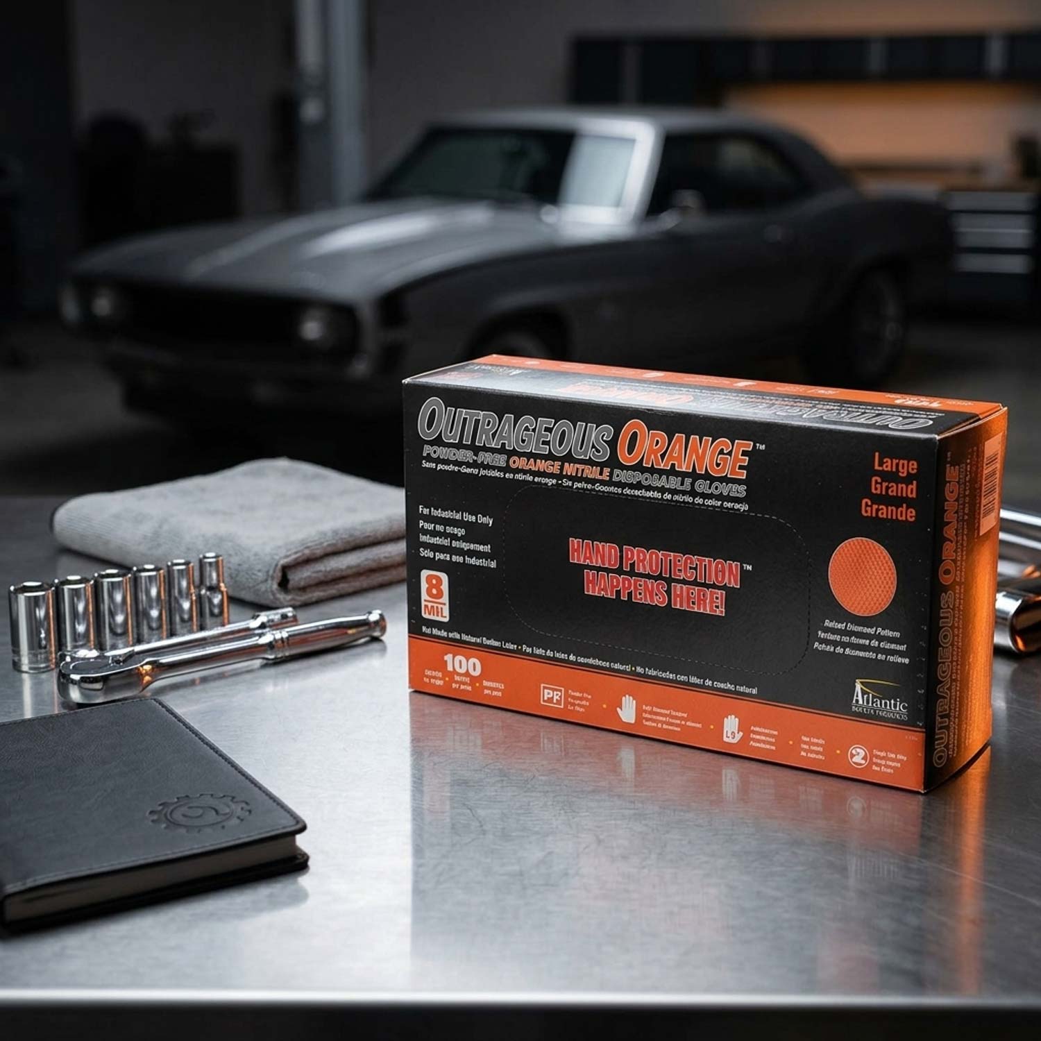 Box of Outrages Orange hand protection gloves on a table with tools and a car in the background