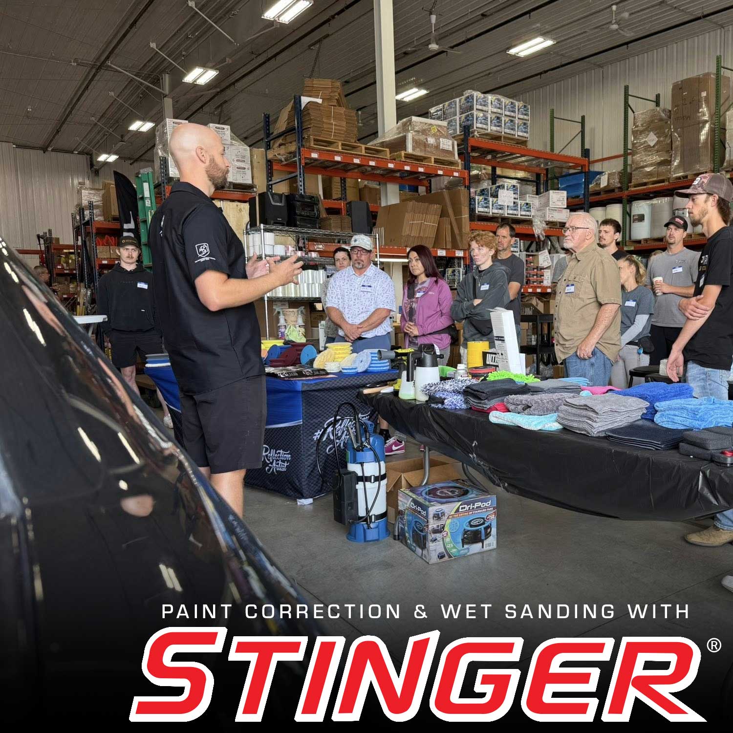 Workshop setting with people around a table, featuring Stinger paint correction equipment.