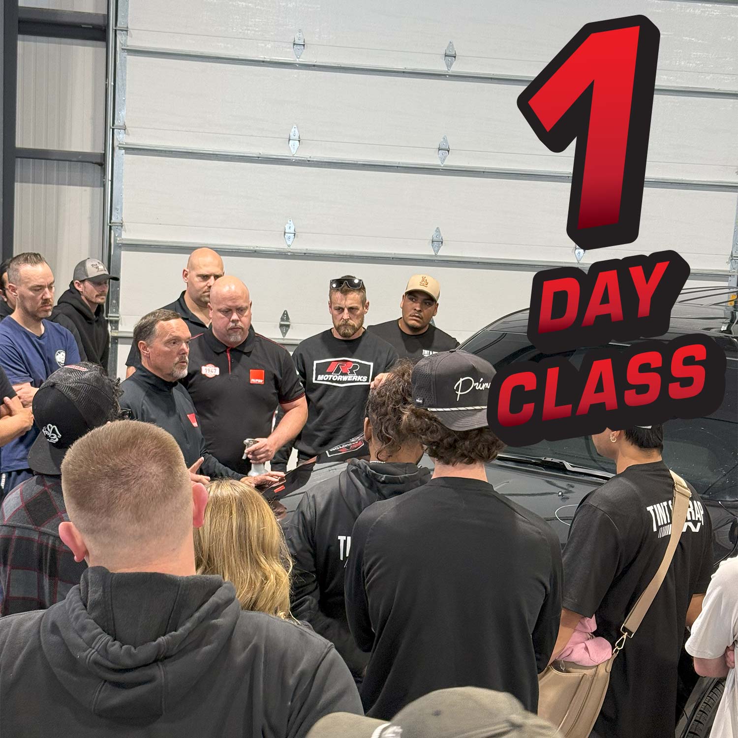Group of people gathered around a car with a '1 Day Class' sign in front.