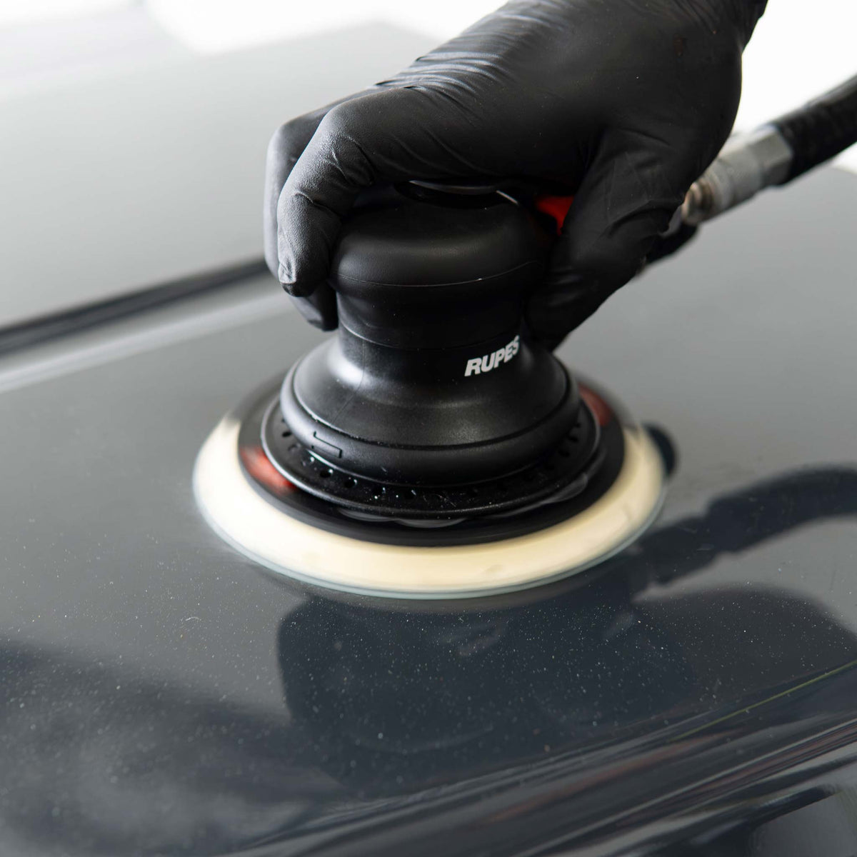 RUPES Skorpio III palm sander running on a black car hood in a body shop