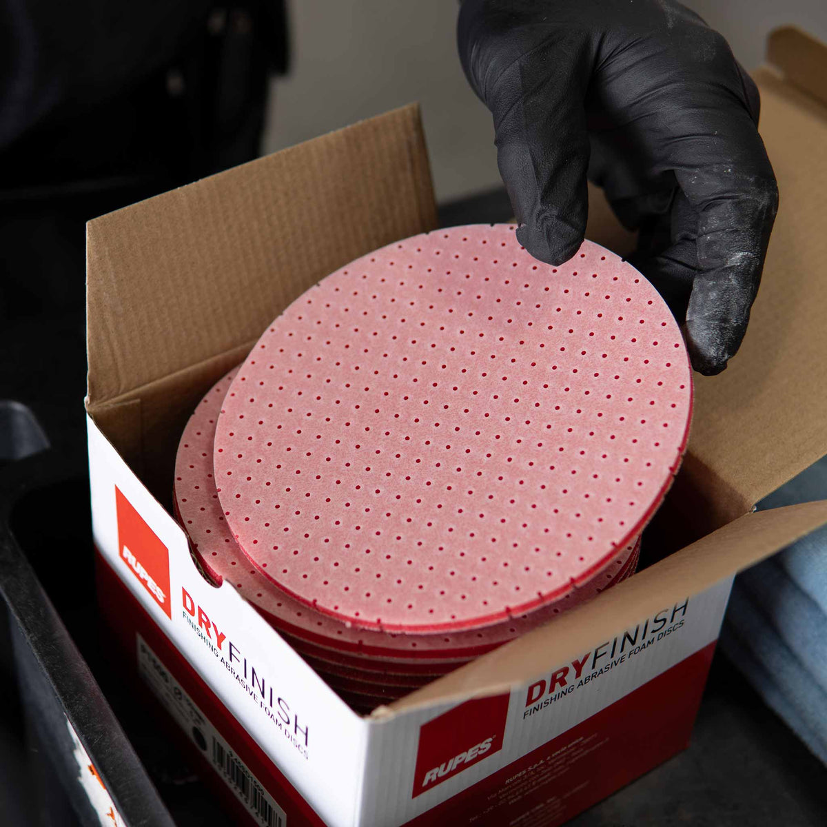 Pulling a red RUPES DryFinish foam disc out of its open box in the shop