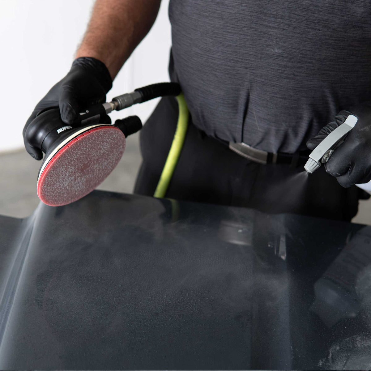 Spraying water on a black panel before wet sanding with a RUPES DryFinish disc