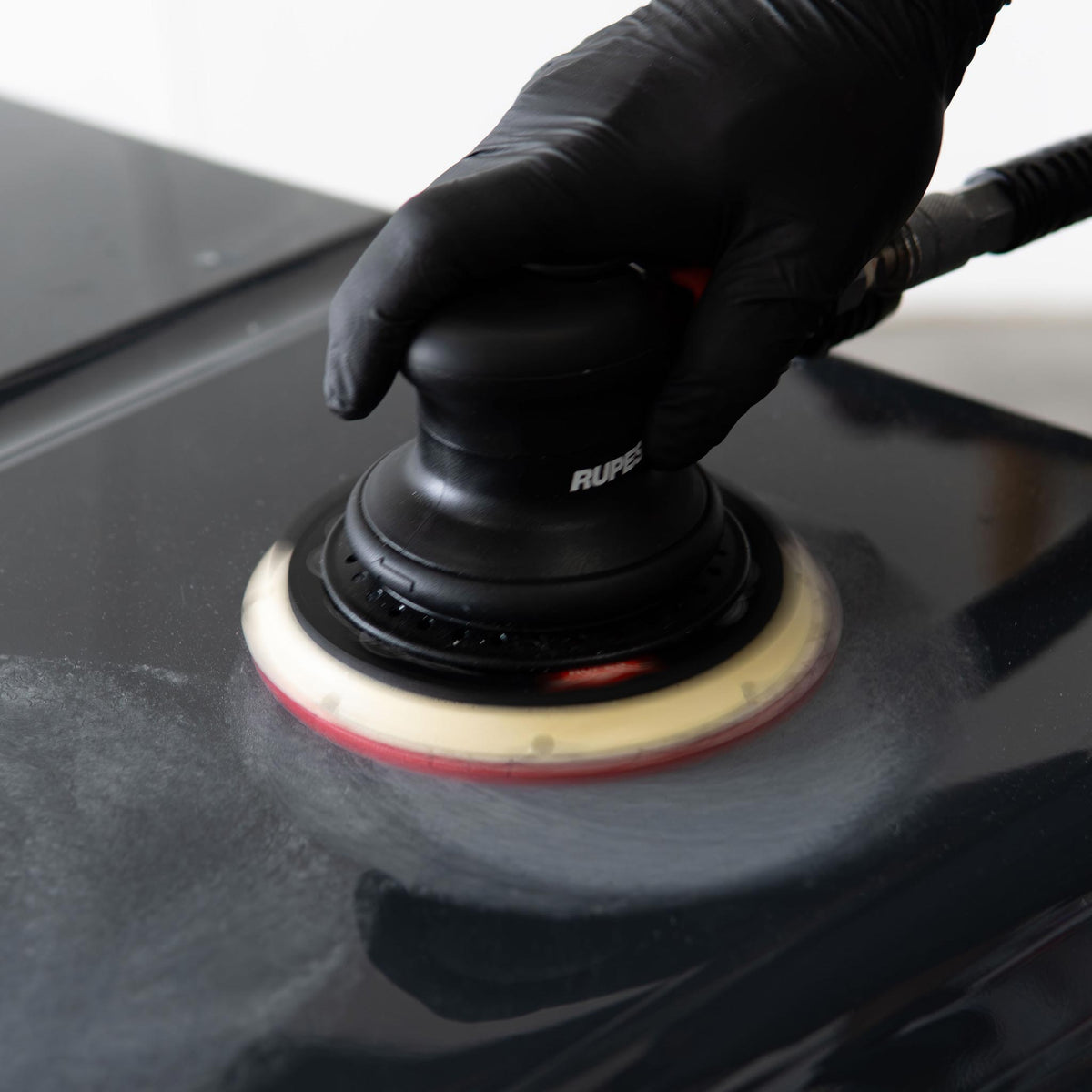 RUPES palm sander dry sanding a black car hood with a red DryFinish foam disc