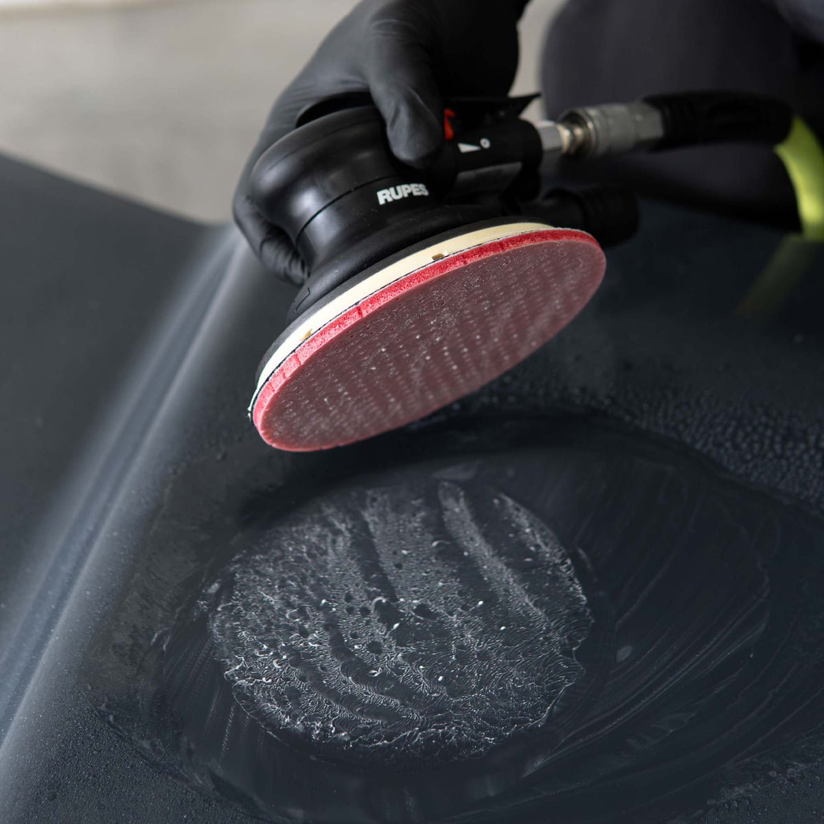 RUPES DryFinish disc lifted off a wet black panel showing the sanding slurry