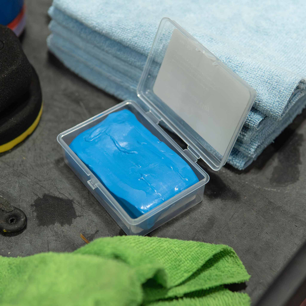 Stinger blue clay bar in its storage case beside microfiber towels on a detail bench