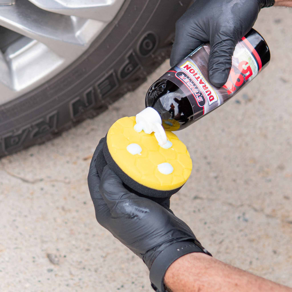 Applying Stinger 591 Duration tire dressing onto the yellow hex pad applicator at the wheel