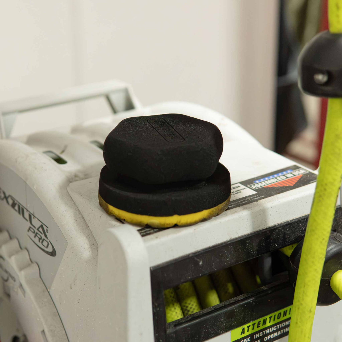 Stinger hex pad tire dressing applicator resting on a pressure washer in a detail shop