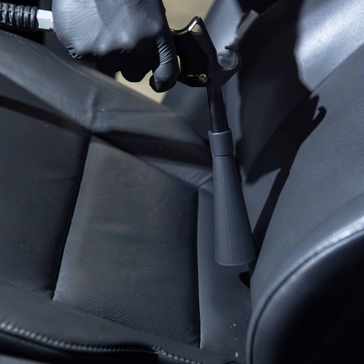 Stinger Twister Blow Gun blowing debris out of a black leather seat seam