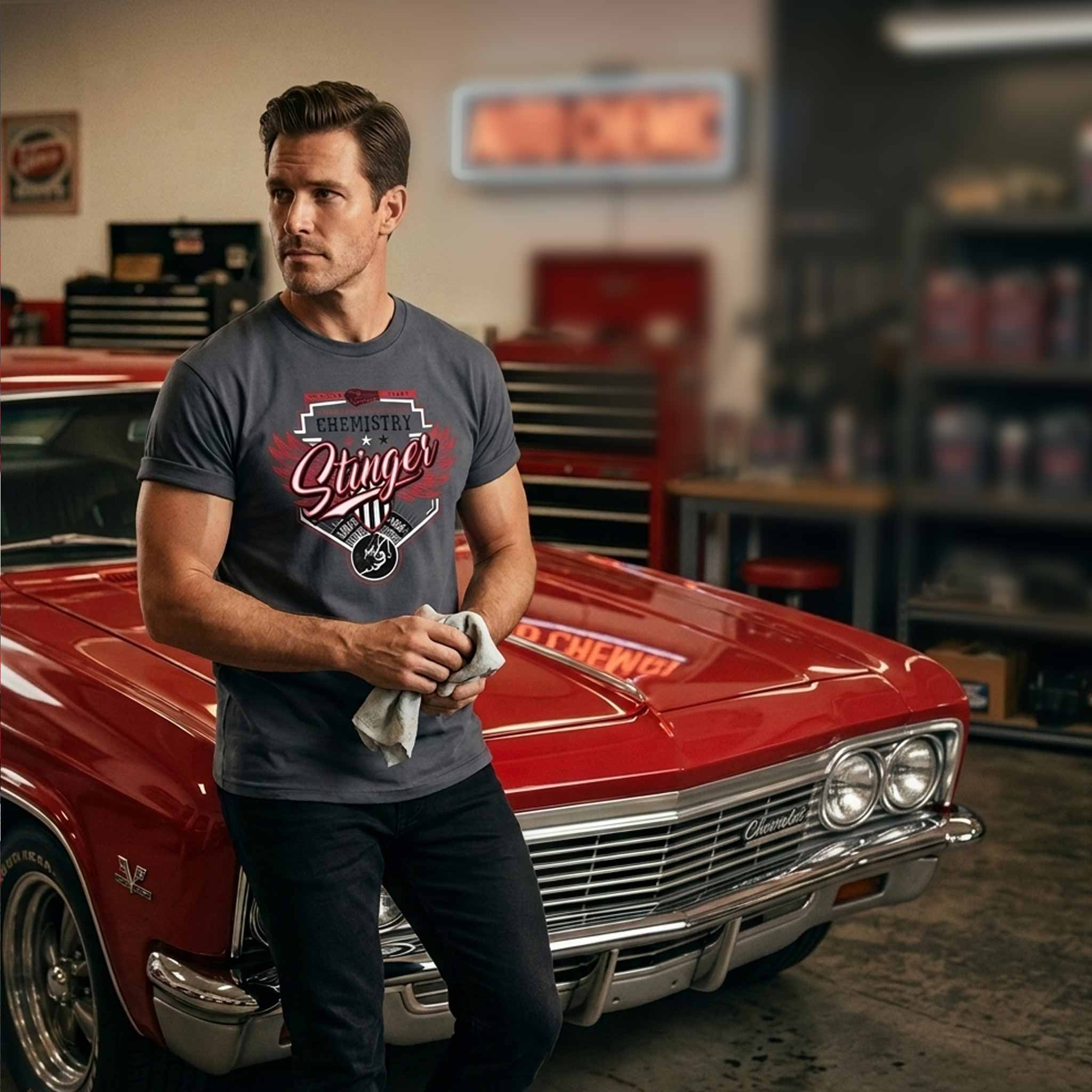 Man standing next to a red classic car displaying a stinger tshirt in a garage setting