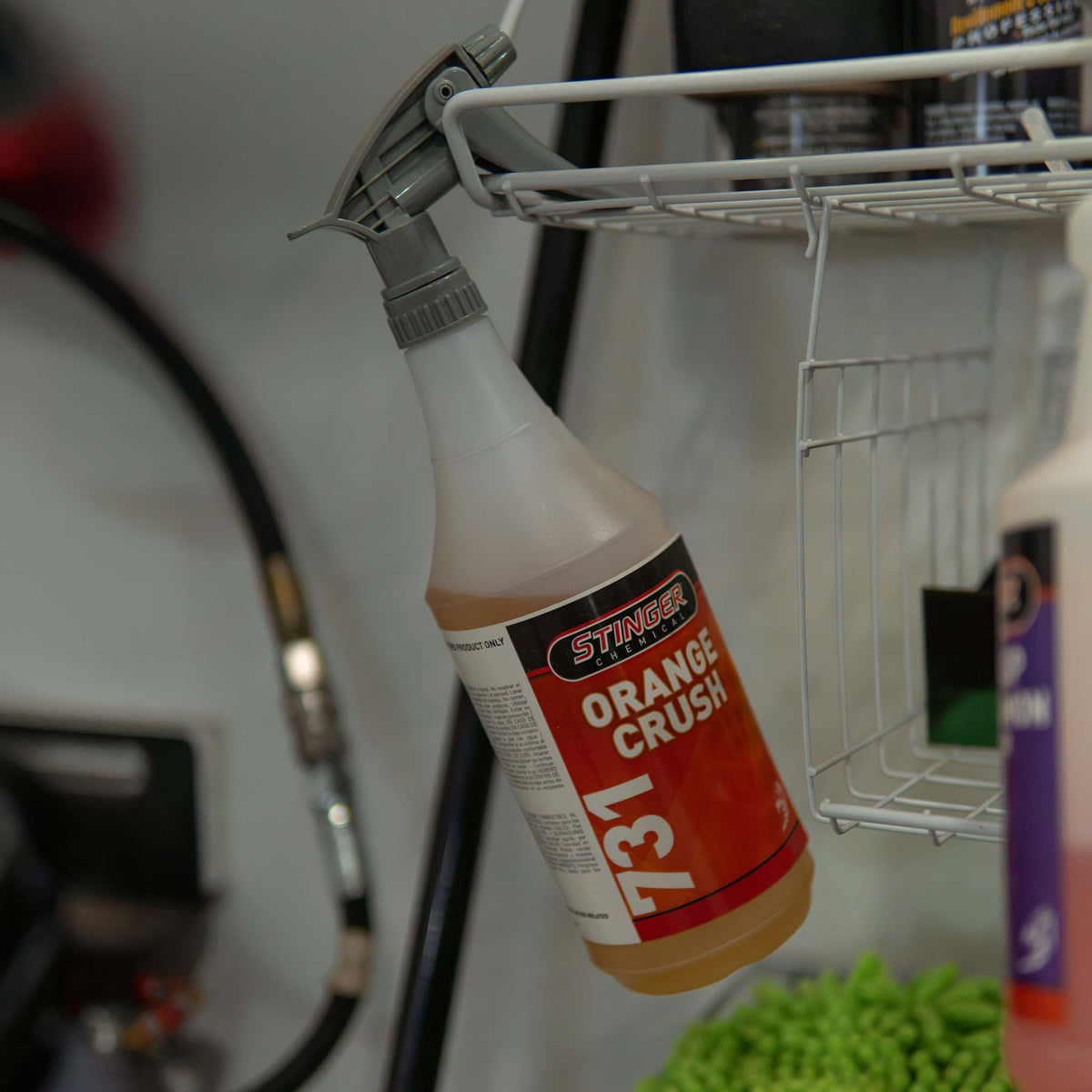 Stinger Chemical Orange Crush 731 solvent degreaser spray bottle hanging on a rack in a detailing bay