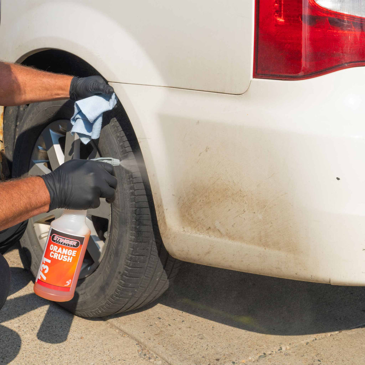 Stinger Chemical Orange Crush 731 tar remover sprayed on tar spots behind a white vehicle's rear wheel