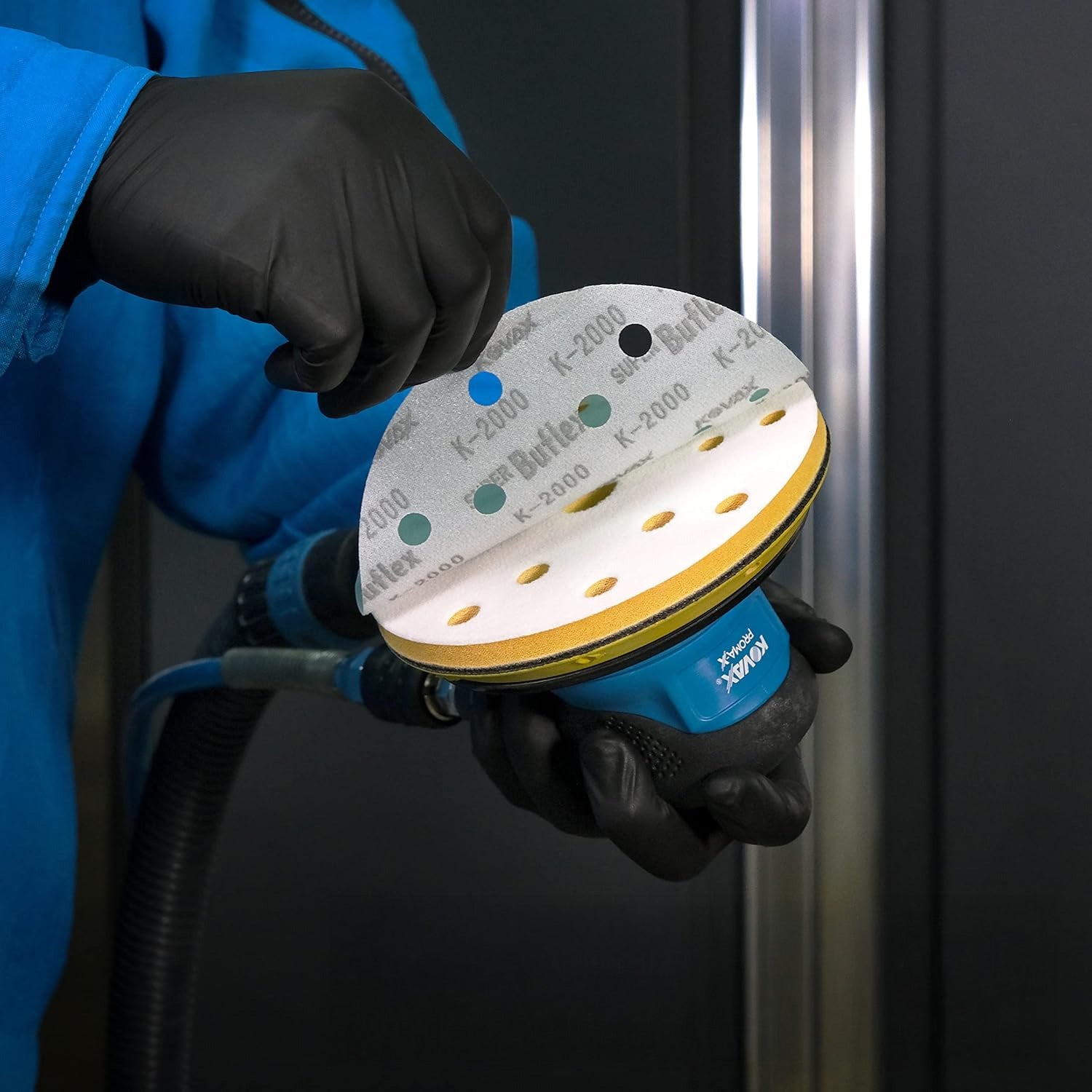Person holding a super buflex sanding disc with a kovax sander against a dark background