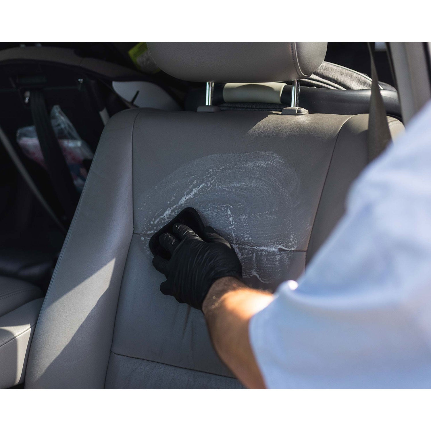 Person cleaning a car seat with a black glove nad interior scrubber
