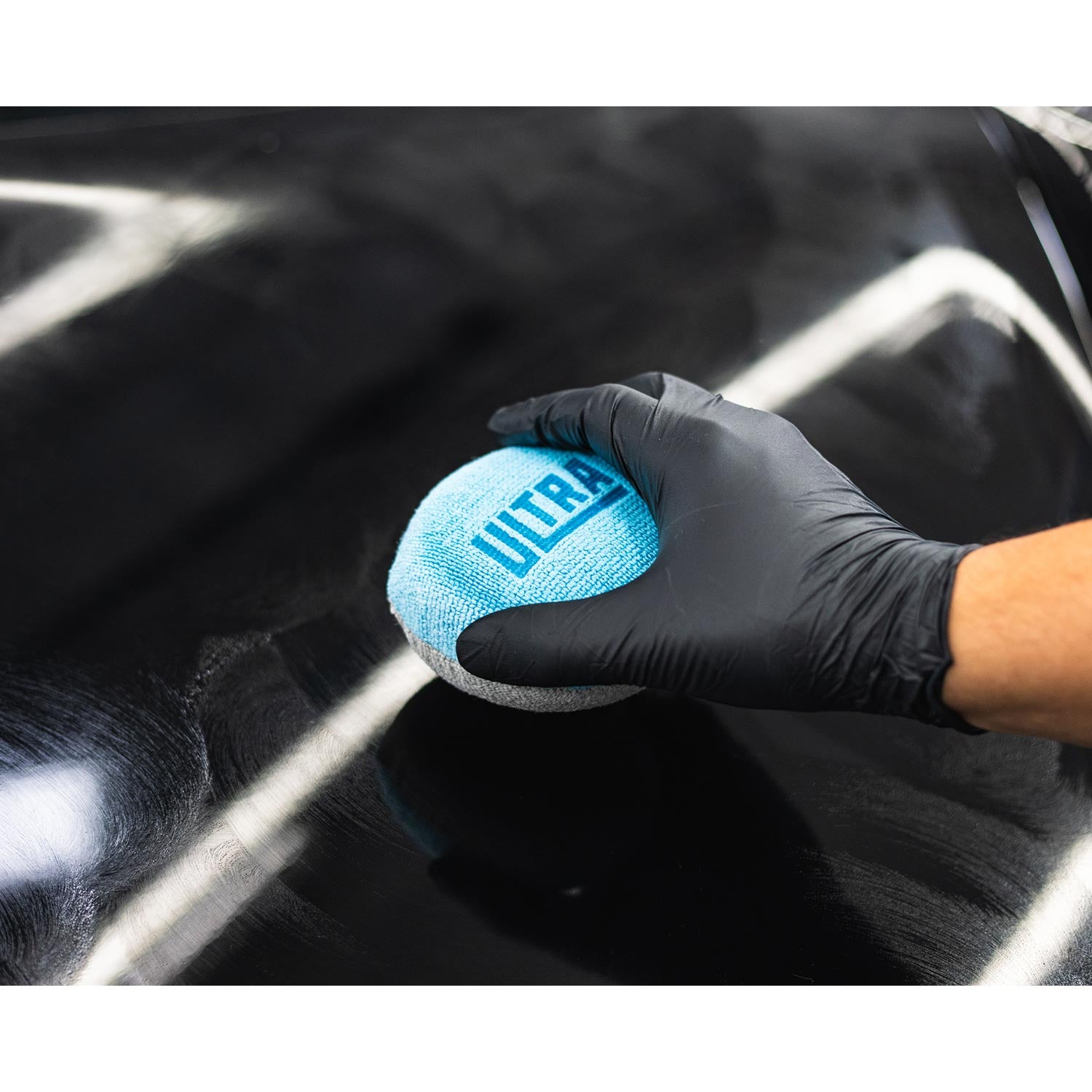 Person holding a blue Ultra microfiber applicator with black gloves applying a coating on a car hood