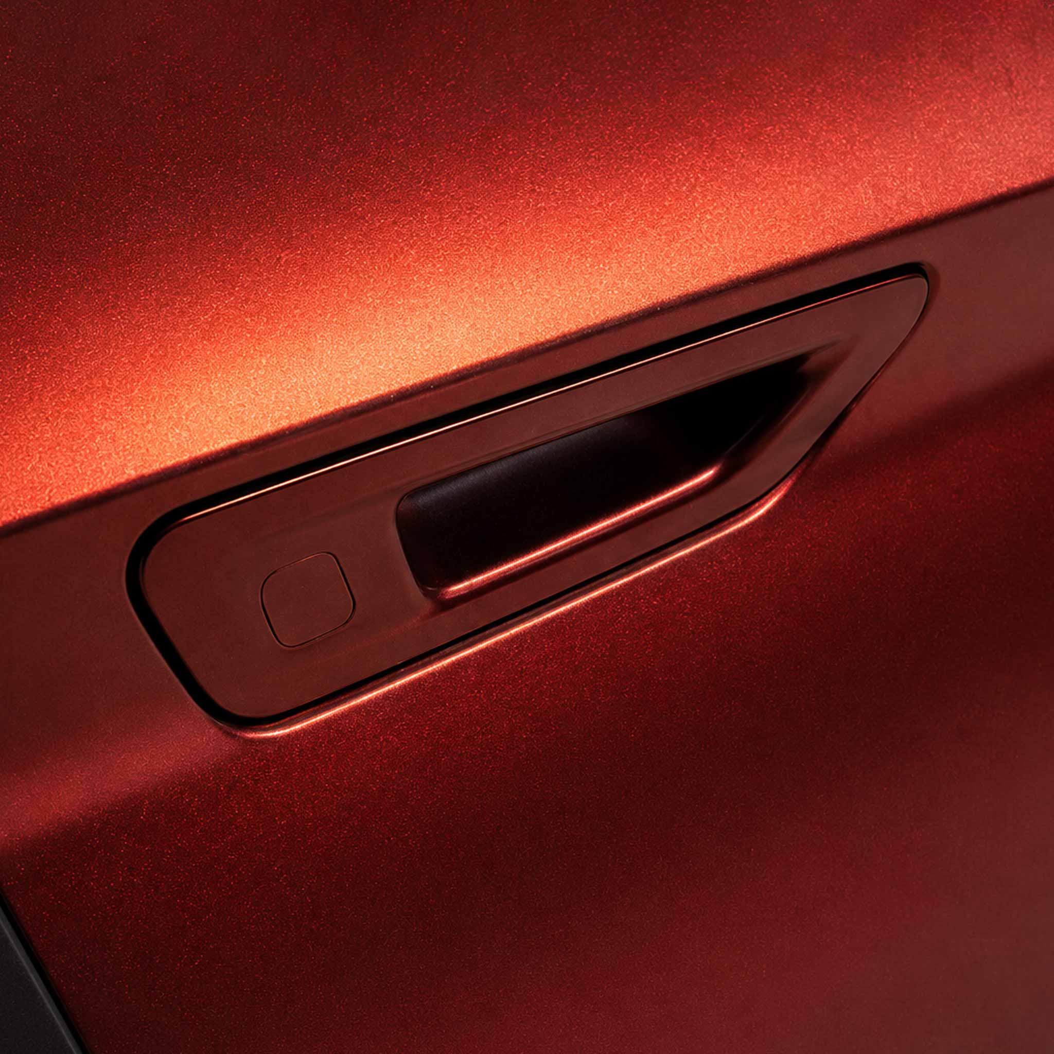 Close-up of a car door handle recessed into a metallic red vehicle body, with a subtle warm orange glow and a dark interior handle opening.